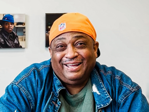 A medium toned man in a yellow hat, blue shirt, and green t-shirt