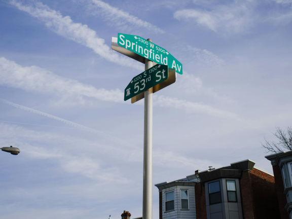 photo of a philly street sign with rowhomes in the background, blue sky