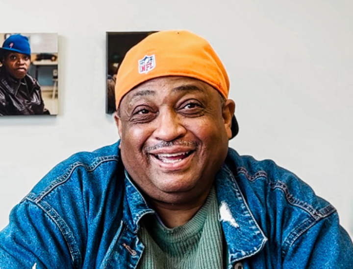 A medium toned man in a yellow hat, blue shirt, and green t-shirt